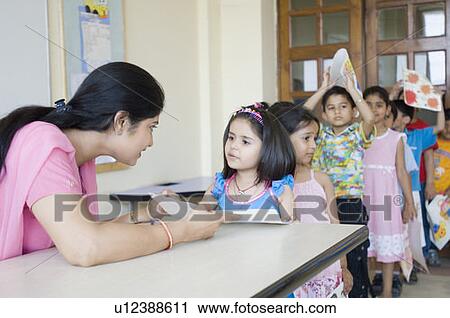 Children standing in a row and a teacher checking their drawings View Large Photo Image Stock Image - Children standing in a row and a teacher checking their drawings. Fotosearch