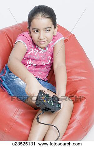 Close-up of a girl sitting on a bean bag and playing a video game View Large Photo Image Stock Image - Close-up of a girl sitting on a bean bag and playing a video game. Fotosearch
