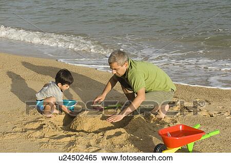 Stock Photography - Mid adult man making a sand castle on the beach with his son. Fotosearch