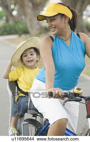 Mid adult woman riding a bicycle with her son sitting behind her View Large Photo Image Picture - Mid adult woman riding a bicycle with her son sitting behind her. Fotosearch