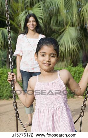 Stock Image - Portrait of a girl on a swing with her mother standing in the background. Fotosearch