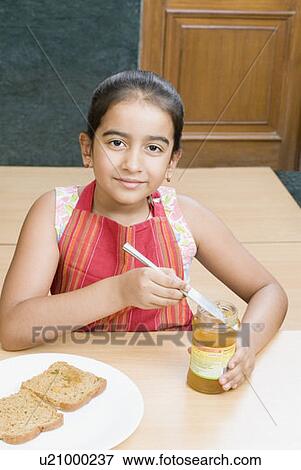 Stock Photo - Portrait of a girl putting a table knife into a jam jar. Fotosearch