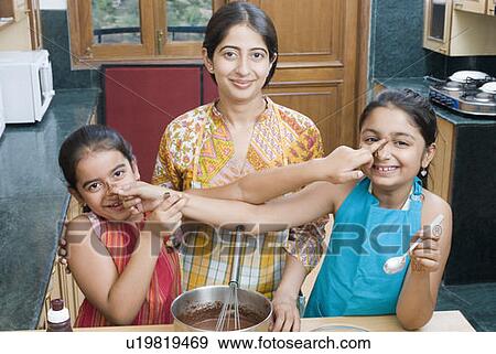 Portrait of a mid adult woman baking chocolate sauce with her daughters touching each other's nose View Large Photo Image Stock Photo - Portrait of a mid adult woman baking chocolate sauce with her daughters touching each other's nose. Fotosearch