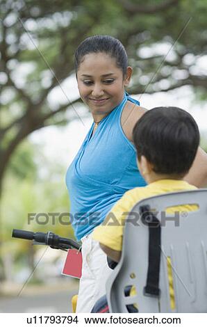 Side profile of a mid adult woman looking at her son riding a bicycle View Large Photo Image Picture - Side profile of a mid adult woman looking at her son riding a bicycle. Fotosearch
