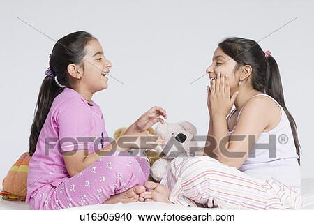 Stock Image - Side profile of two girls sitting and playing together. Fotosearch