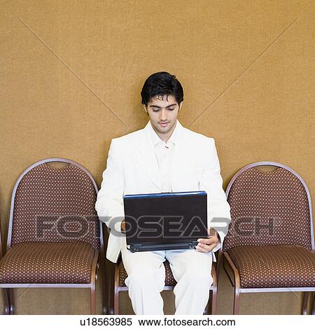 Businessman sitting on a chair and using a laptop View Large Photo Image Stock Photography - Businessman sitting on a chair and using a laptop. Fotosearch
