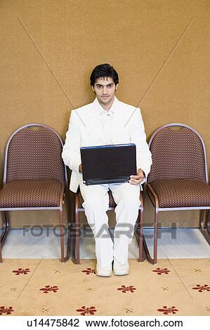 Stock Image - Portrait of a businessman sitting on a chair and using a laptop. Fotosearch