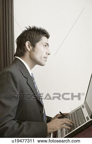 Stock Image - Side profile of a businessman using a laptop on a lectern. Fotosearch