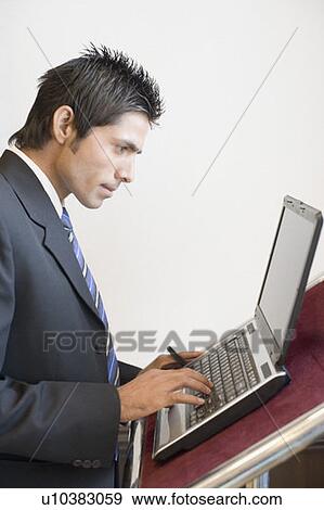 Side profile of a businessman using a laptop at a lectern View Large Photo Image Stock Photo - Side profile of a businessman using a laptop at a lectern. Fotosearch