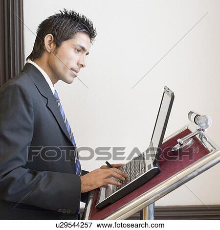 Stock Photo - Side profile of a businessman using a laptop on a lectern. Fotosearch