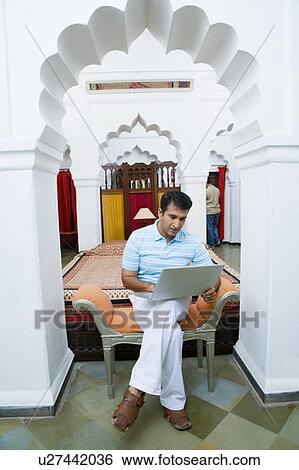 Stock Photograph - Mid adult man sitting on a couch and using a laptop. Fotosearch