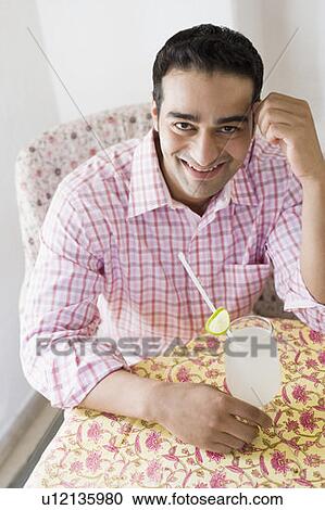 Stock Image - Portrait of a young man sitting at a table and smiling. Fotosearch