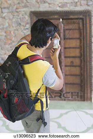 Stock Image - Rear view of a young man taking a photograph. Fotosearch
