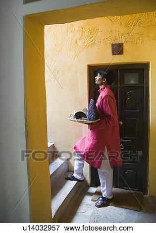 Stock Photo - Side profile of a waiter carrying a teapot in a tray and moving up on a staircase. Fotosearch