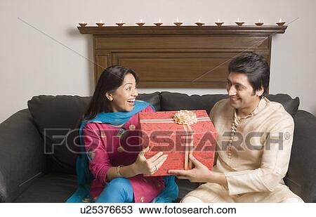 Stock Image - Close-up of a couple holding a diwali gift and smiling. Fotosearch