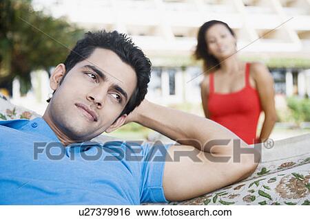 Stock Photograph - Close-up of a young man lying in a hammock with a young woman behind him. Fotosearch