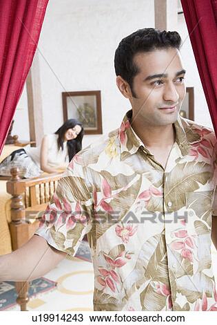 Close-up of a young man smirking with a young woman lying on the bed in the background View Large Photo Image Stock Image - Close-up of a young man smirking with a young woman lying on the bed in the background. Fotosearch