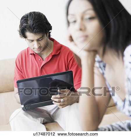 Stock Image - Close-up of a young woman thinking with a young man using a laptop beside her. Fotosearch