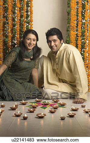 Stock Image - Mid adult man and a young woman sitting in front of oil lamps. Fotosearch