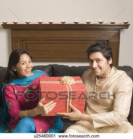 Stock Image - Portrait of a couple holding a diwali gift and smiling. Fotosearch