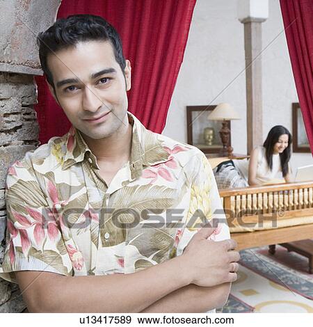 Stock Photo - Portrait of a young man smiling with a young woman lying on the bed in the background. Fotosearch