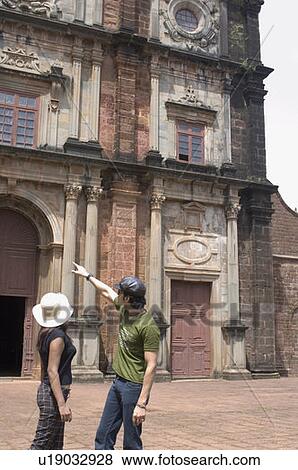 Stock Photo - Side profile of a young couple standing in front of a building, Goa, India. Fotosearch