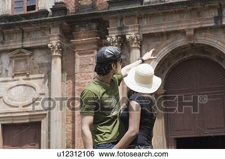 Side profile of a young man standing with a young woman and pointing towards a building, Goa, India View Large Photo Image Stock Photograph - Side profile of a young man standing with a young woman and pointing towards a building, Goa, India. Fotosearch