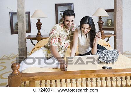 Stock Image - Young couple using a laptop on the bed. Fotosearch