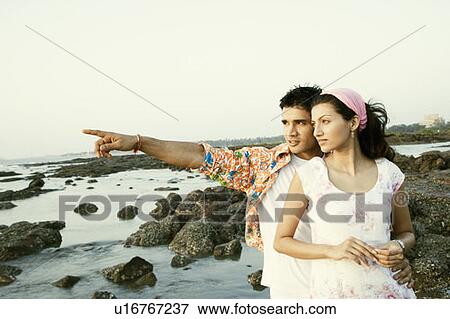 Young man pointing away to a young woman and standing on the beach View Large Photo Image Stock Photo - Young man pointing away to a young woman and standing on the beach. Fotosearch