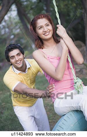 Stock Image - Young man pushing a young woman on a tire swing. Fotosearch