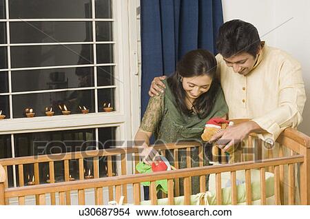 Young woman and a mid adult man looking inside a crib and smiling View Large Photo Image Picture - Young woman and a mid adult man looking inside a crib and smiling. Fotosearch