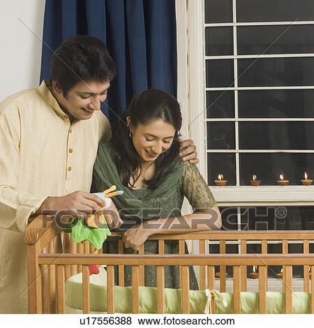 Young woman and a mid adult man looking inside a crib and smiling View Large Photo Image Stock Photo - Young woman and a mid adult man looking inside a crib and smiling. Fotosearch