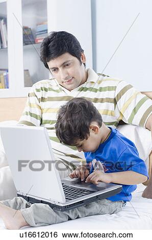 Boy using a laptop with his father sitting beside him View Large Photo Image Stock Photograph - Boy using a laptop with his father sitting beside him. Fotosearch