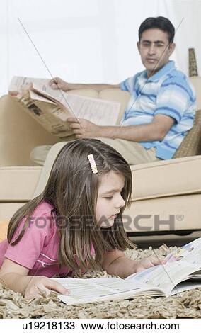 Girl reading a book with her father holding a newspaper in the background View Large Photo Image Stock Image - Girl reading a book with her father holding a newspaper in the background. Fotosearch