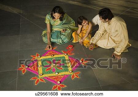Stock Photo - High angle view of a mid adult man and a young woman making a rangoli with their daughter. Fotosearch