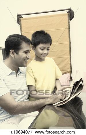 Stock Photo - Mid adult man reading a newspaper with his son and smiling. Fotosearch