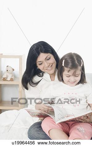 Mid adult woman reading a book with her daughter and smiling View Large Photo Image Stock Photograph - Mid adult woman reading a book with her daughter and smiling. Fotosearch