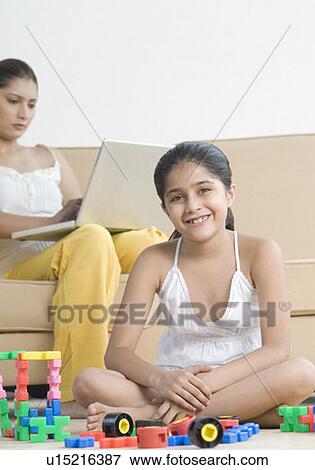 Portrait of a girl playing with building blocks and her mother using a laptop behind her View Large Photo Image Stock Photo - Portrait of a girl playing with building blocks and her mother using a laptop behind her. Fotosearch