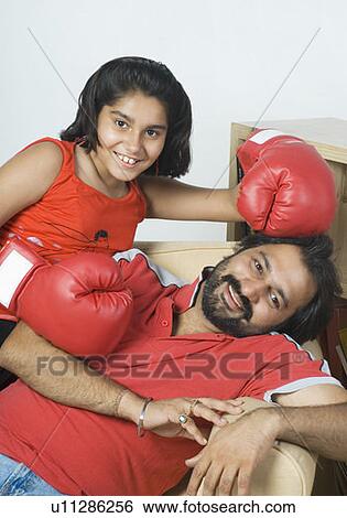 Portrait of a mid adult man reclining on a couch with his daughter wearing boxing gloves View Large Photo Image Stock Photograph - Portrait of a mid adult man reclining on a couch with his daughter wearing boxing gloves. Fotosearch