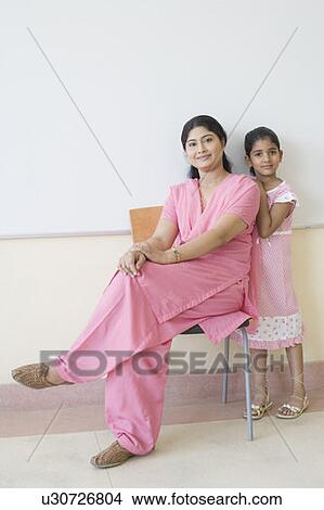 Picture - Portrait of a teacher sitting on a chair with a schoolgirl standing beside her. Fotosearch
