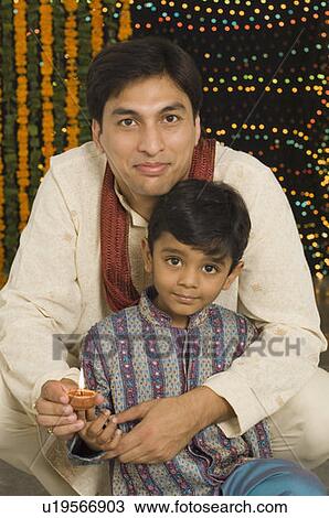 Stock Image - Portrait of a young man and his son holding diwali lamps. Fotosearch