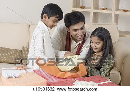 Stock Image - Young man opening a gift in front of his children. Fotosearch