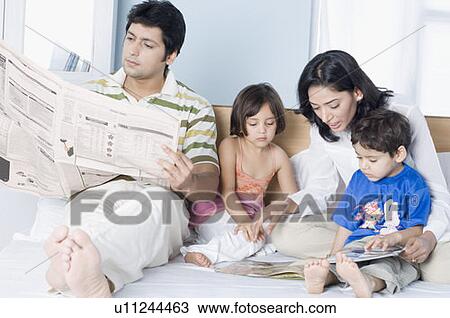 Young woman showing a magazine to her children with her husband reading a newspaper beside them View Large Photo Image Stock Image - Young woman showing a magazine to her children with her husband reading a newspaper beside them. Fotosearch