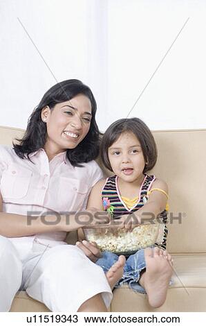 Stock Image - Young woman sitting with her daughter on a couch and smiling. Fotosearch