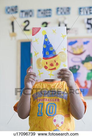 Close-up of a schoolboy hiding his face with a drawing View Large Photo Image Stock Photo - Close-up of a schoolboy hiding his face with a drawing. Fotosearch