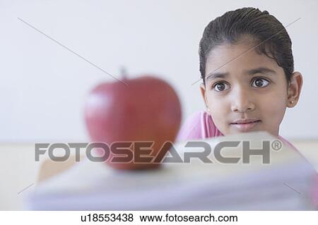 Stock Photo - Close-up of an apple on books with a schoolgirl in the background. Fotosearch