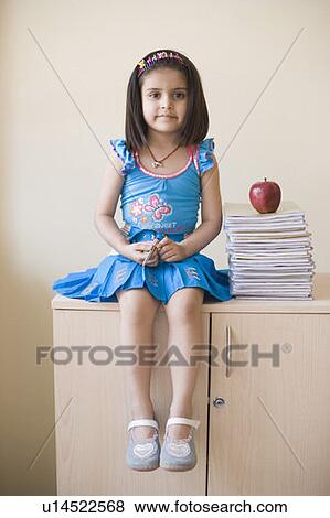 Portrait of a girl sitting near a stack of books on a cabinet View Large Photo Image Stock Photo - Portrait of a girl sitting near a stack of books on a cabinet. Fotosearch