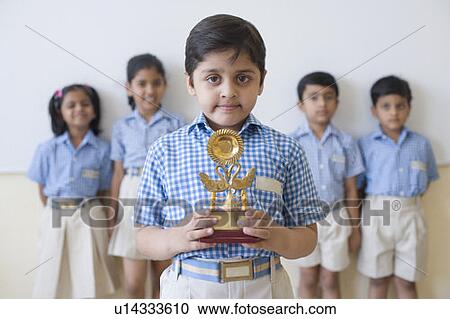 Portrait of a schoolboy holding a trophy with his classmates in the background View Large Photo Image Stock Image - Portrait of a schoolboy holding a trophy with his classmates in the background. Fotosearch