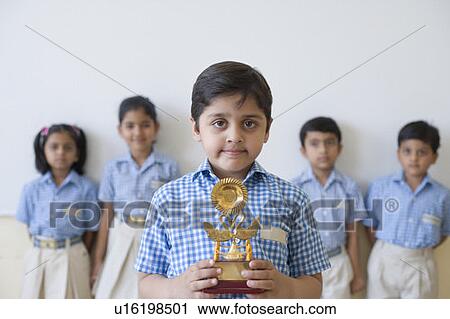 Portrait of a schoolboy holding a trophy with his classmates in the background View Large Photo Image Stock Image - Portrait of a schoolboy holding a trophy with his classmates in the background. Fotosearch