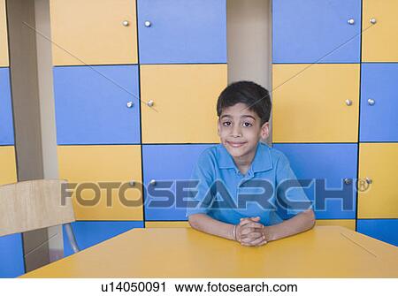 Portrait of a schoolboy sitting at a table and smirking View Large Photo Image Stock Image - Portrait of a schoolboy sitting at a table and smirking. Fotosearch